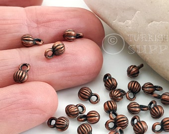 May include: A close-up of a pile of small, copper-colored metal beads with a loop on top. The beads have a ribbed texture and are about 1/2 inch in diameter.