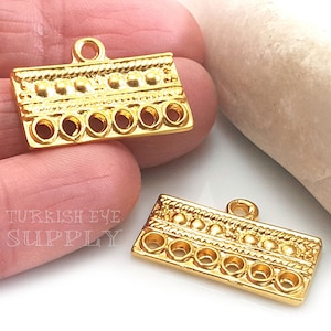 Può includere: Due ciondoli pendenti in metallo dorato con un design decorativo e cinque fori per infilare perline. I ciondoli hanno un anello in alto per essere attaccati a una collana o un braccialetto.