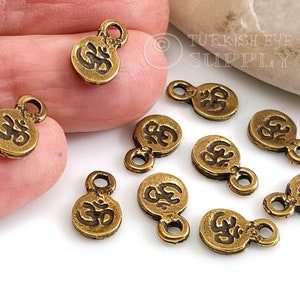 Puede incluir: Diez abalorios de metal dorado con el símbolo Om grabado en cada uno. Los abalorios tienen un pequeño bucle en la parte superior para sujetarlos a joyas u otras manualidades.