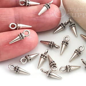 May include: Silver-toned metal cone-shaped charms with a loop at the top for jewelry making. The charms have a textured design around the loop and base of the cone. The image shows multiple charms scattered on a white surface.