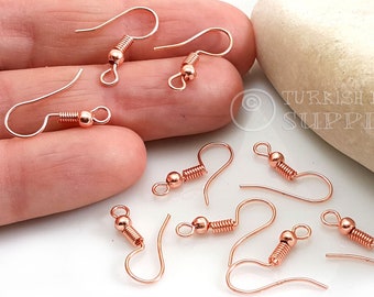 May include: A close-up of ten rose gold earring hooks with a spring coil. The hooks are on a white surface.