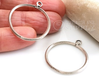 Könnte beinhalten: Zwei silberfarbene Metall-Kreis-Anhänger-Rahmen mit einer kleinen Schlaufe oben. Die Rahmen sind leicht strukturiert und haben eine gehämmerte Oberfläche.
