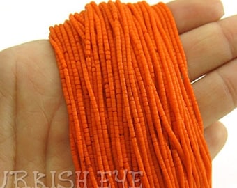 May include: A bundle of vibrant orange seed beads, tightly strung together. The beads are held in a hand, showcasing their color and texture. The beads appear to be small and cylindrical, suitable for jewelry making or crafts.