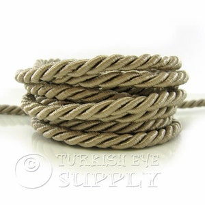 May include: A close-up of a beige twisted cord, coiled into a circle. The cord is made of a soft, silky material and has a subtle sheen.