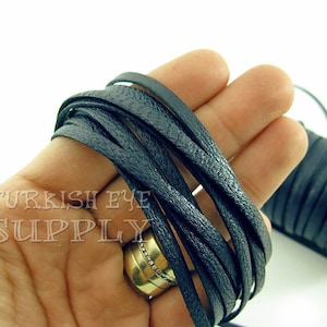 May include: Black leather cord, approximately 5mm wide, wound around a spool. The cord is soft and supple, with a slightly textured surface.