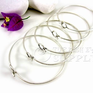 May include: Five silver bangle bracelets with a simple, open-circle design and a small, hinged clasp. The bracelets are stacked on top of each other, with the text "TURKISH EYE SUPPLY" visible in the background.