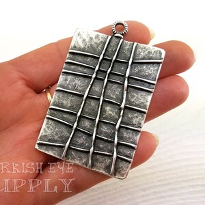 May include: A silver pendant with a textured, grid-like design. The pendant has a loop at the top for attaching a chain.