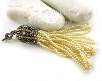 May include: A cream-colored beaded tassel with a gold-toned metal top adorned with clear rhinestones. The tassel is approximately 6 inches long.