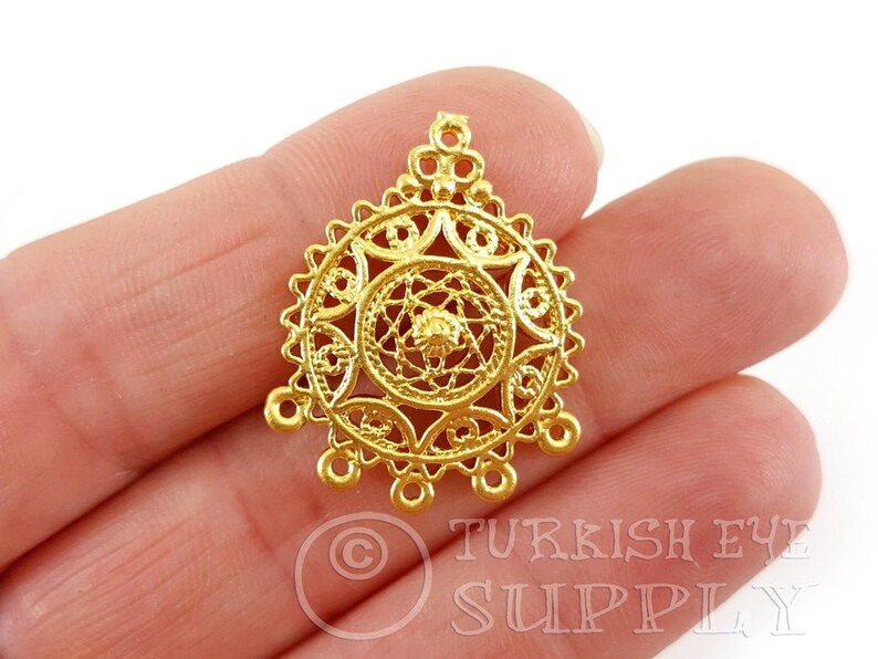 May include: Gold filigree pendant featuring a circular design with three loops at the bottom. The pendant is crafted from metal and boasts a delicate, intricate pattern.