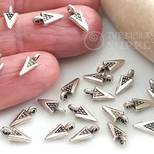 Puede incluir: Encantos de punta de flecha plateados con una superficie texturizada. Los encantos tienen un bucle en la parte superior para sujetarlos a joyas u otras manualidades.