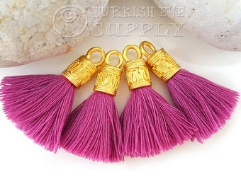 May include: Four purple tassel charms with gold metal caps. Each cap has an ornate design and a loop for attaching to a project.