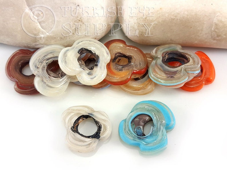 May include: Assortment of eight colorful glass flower-shaped beads with a hole in the center. The beads are made of layered glass with different colors and patterns.