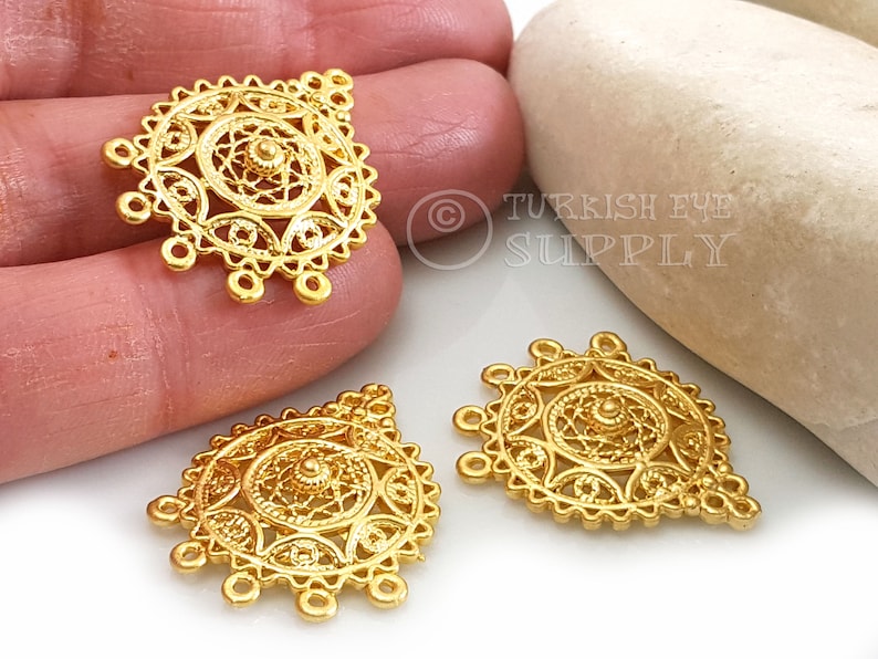 May include: Three gold-coloured metal pendants with intricate filigree designs. Each pendant features a circular centre with a smaller circle in the middle. The pendants have five loops at the bottom.