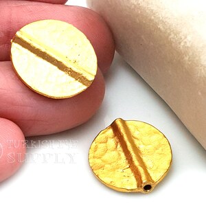 以下が含まれることがあります： テクスチャ加工された表面と対角線の溝がある、2つの金色の丸い金属ビーズ。ビーズは白い背景に表示されています。ビーズはおそらくジュエリー作りのためです。