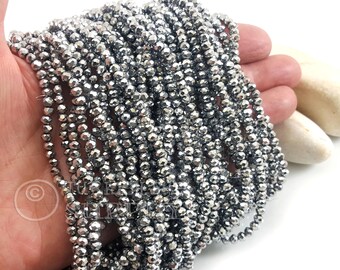 May include: Strands of faceted, metallic gray beads. The beads are small and round, strung together to create multiple strands. The beads have a reflective surface, catching the light and creating a shimmering effect. The beads are held in a hand.