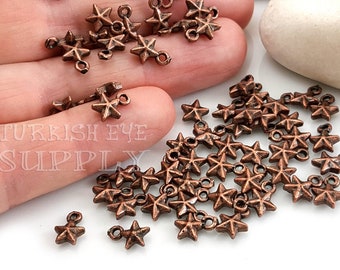 Könnte beinhalten: Ein Haufen kupferfarbener sternförmiger Charms mit Sprungringen. Die Charms sind etwa 1 cm groß und haben eine rustikale Oberfläche.