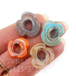 May include: Four agate flower beads in different colors: gray, blue, orange, and beige. Each bead has a hole in the center and a swirling pattern.