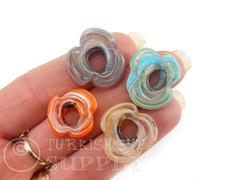 May include: Four agate flower beads in different colors: gray, blue, orange, and beige. Each bead has a hole in the center and a swirling pattern.
