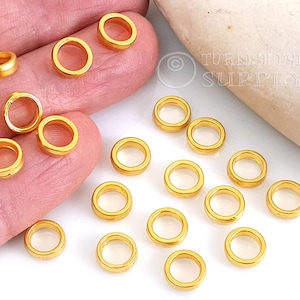 May include: A close-up of 18 gold jump rings, which are small metal rings used for connecting jewelry components. The rings are scattered on a white surface.