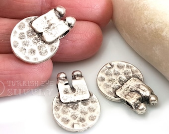 Peut inclure: Trois breloques rondes en métal argenté avec une surface texturée et une boucle sur le dessus. La boucle est en forme de U avec deux petites boules rondes sur le dessus.