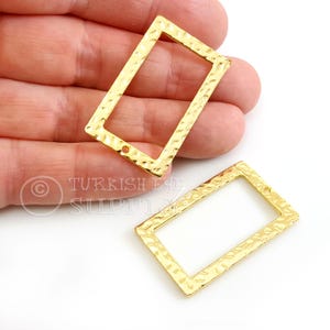 Può includere: Due elementi di gioielleria rettangolari in metallo dorato con una texture martellata. Ogni elemento ha una forma rettangolare con un foro a un'estremità. Gli elementi sono esposti su sfondo bianco.