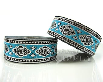 Puede incluir: Dos rollos de ribete azul turquesa con diseños florales negros y plateados. El ribete tiene un borde de cuentas plateadas y negras.