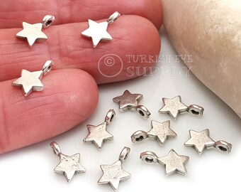 May include: A close-up of silver star-shaped charms with a loop at the top. The charms are scattered on a white surface.  Turkish Eye Supply is printed on the surface.