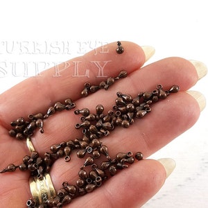 May include: A large quantity of small, teardrop-shaped metal charms in a copper color. The charms have a loop at the top for attaching to jewelry or other crafts.