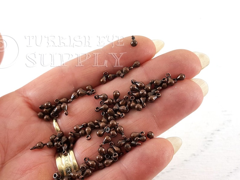 May include: A large quantity of small, teardrop-shaped metal charms in a copper color. The charms have a loop at the top for attaching to jewelry or other crafts.