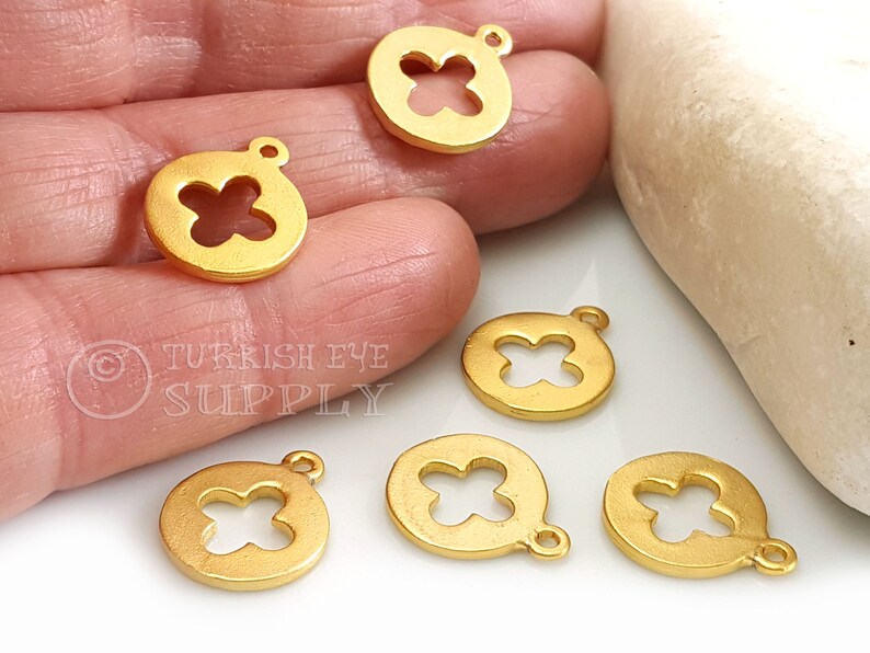 May include: Six gold-toned metal charms with a four-leaf clover design. Each charm has a loop for attaching to a necklace or bracelet.