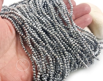 May include: Strands of small, faceted, silver-colored beads. The beads are strung together, creating multiple strands. The beads have a reflective surface, catching the light and creating a sparkling effect. The beads are held in a hand.