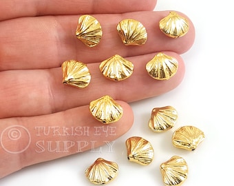 Può includere: Una collezione di piccole perline dorate a forma di conchiglia. Ogni perlina presenta una texture dettagliata e scanalata e un piccolo foro per l'infilatura. Le perline sono esposte su uno sfondo chiaro.