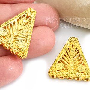 May include: Two gold-tone triangle-shaped metal embellishments with intricate filigree designs. The embellishments have a textured surface and are perfect for adding a touch of elegance to jewellery or crafts.