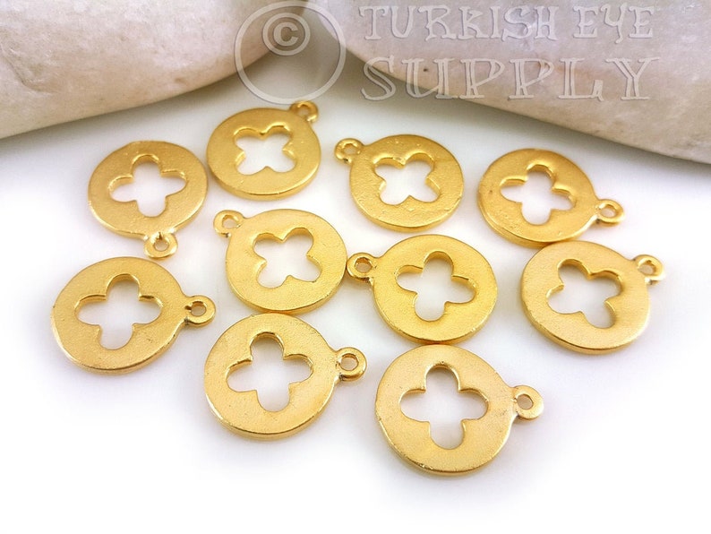 May include: Ten gold-tone metal charms with a circular shape and a four-leaf clover cutout design. Each charm has a small loop for attaching to jewelry or other crafts.