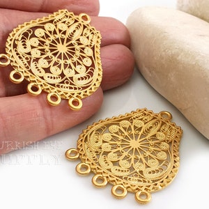 May include: Two gold filigree pendant charms with a circular design and four loops at the bottom. The charms are on a white surface.
