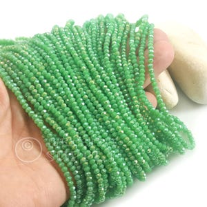 May include: A collection of small, green faceted beads. The beads are strung together and have a shimmering, iridescent finish. The beads are a light green colour. These beads are likely for jewellery making.