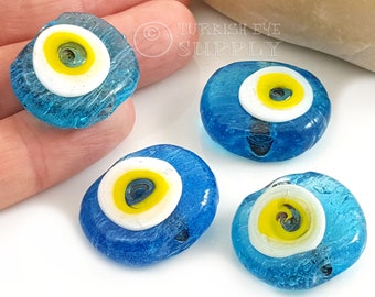 May include: Four blue glass evil eye beads with white and yellow centers. The beads are round and have a textured surface.