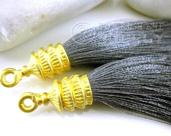 May include: Two gray tassel ends with gold metal tips. The tips have a decorative, ornate design.  The tassels are made of soft, silky fibers.