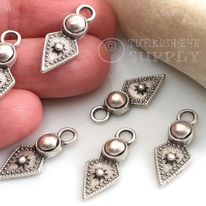 May include: Six silver-toned metal charms with a diamond-shaped design and a round bead at the top. Each charm has a small loop at the top for attaching to jewelry or other crafts.