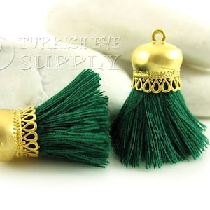 May include: Two green tassel ornaments with gold metal tops. The tops have a decorative design and a loop for hanging.