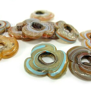 May include: A collection of colorful glass flower-shaped beads with a hole in the center. The beads are made of layered glass in shades of brown, orange, white, and blue.