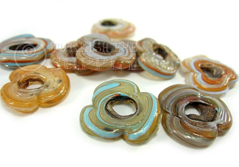 May include: A collection of colorful glass flower-shaped beads with a hole in the center. The beads are made of layered glass in shades of brown, orange, white, and blue.