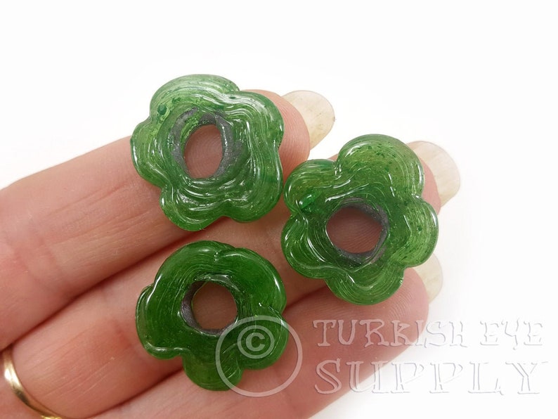 May include: Three green glass flower-shaped beads with a hole in the center. The beads have a swirl pattern and a translucent finish.