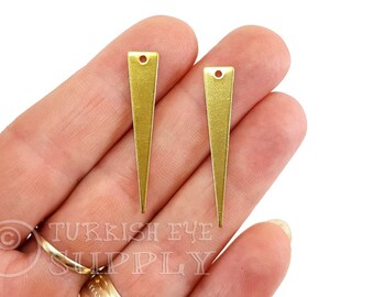 May include: Two gold-colored metal triangle-shaped pendants with a hole at the top. The pendants are about 1.5 inches long.