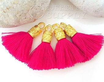 May include: Four bright pink tassel charms with gold metal caps. Each cap has an ornate design and a loop for attaching to a project.