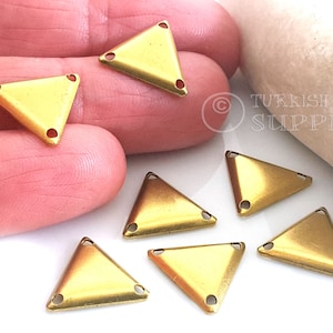 Puede incluir: Siete adornos metálicos de forma triangular de color dorado con tres agujeros cada uno. Los adornos miden aproximadamente 2,5 cm de lado.