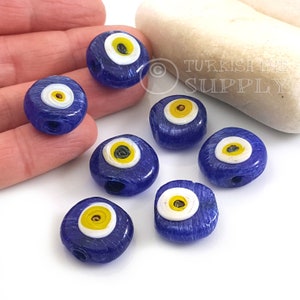 May include: Seven blue glass evil eye beads with white and yellow details. The beads are all the same size and shape, and they are arranged in a circle.