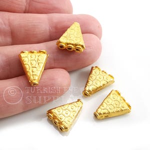 May include: A collection of gold-coloured, triangular jewellery components. Each piece has a honeycomb pattern and three holes at the base. These components are likely for jewellery making, such as earrings or pendants.