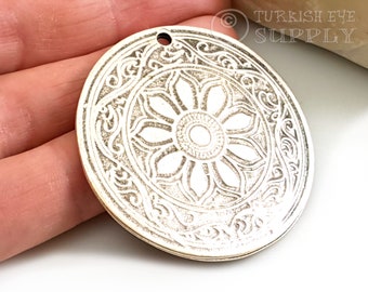 May include: Silver-toned metal pendant with an intricate floral design. The pendant is round and has a hole at the top for hanging.