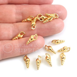 Puede incluir: Encantos de metal de color dorado en forma de concha marina con un bucle para sujetar a joyas u otras manualidades. Los encantos miden aproximadamente 2,5 cm de largo y tienen un diseño detallado de concha marina.